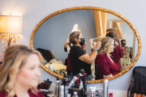 A candid bride preparing for her wedding, getting her hair done in front of a mirror.