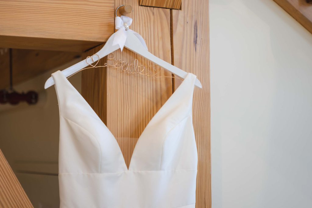 A detailed white wedding dress hangs on a wooden hanger.