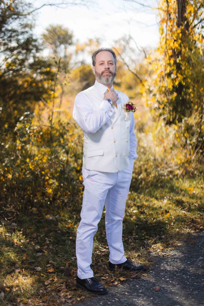 A man in a white suit is posing for a wedding portrait.