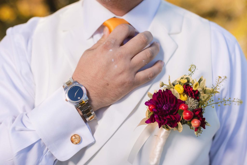 A man is adjusting his boutonniere for a wedding portrait.