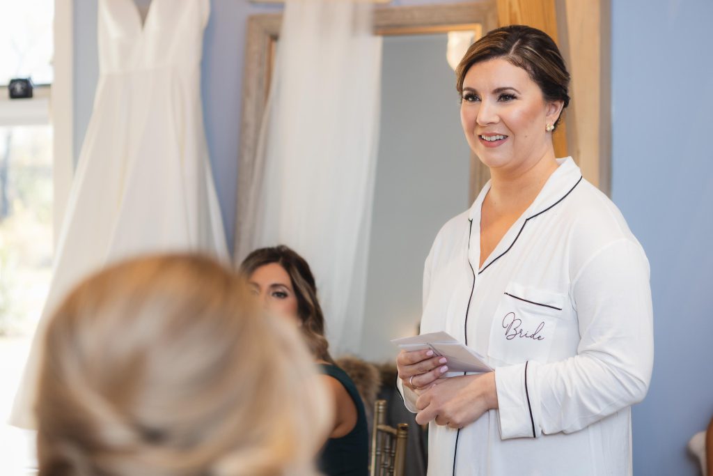 A candid bride preparing for her wedding with her bridesmaids in front of a mirror.
