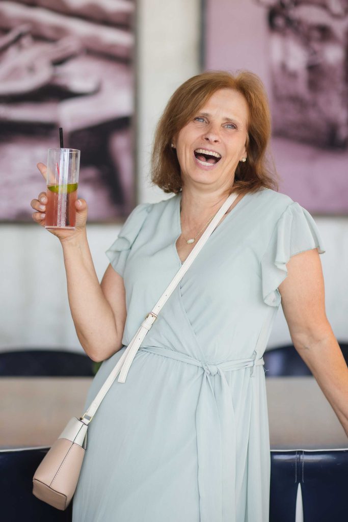 A woman smiling at a birthday party while holding a drink.