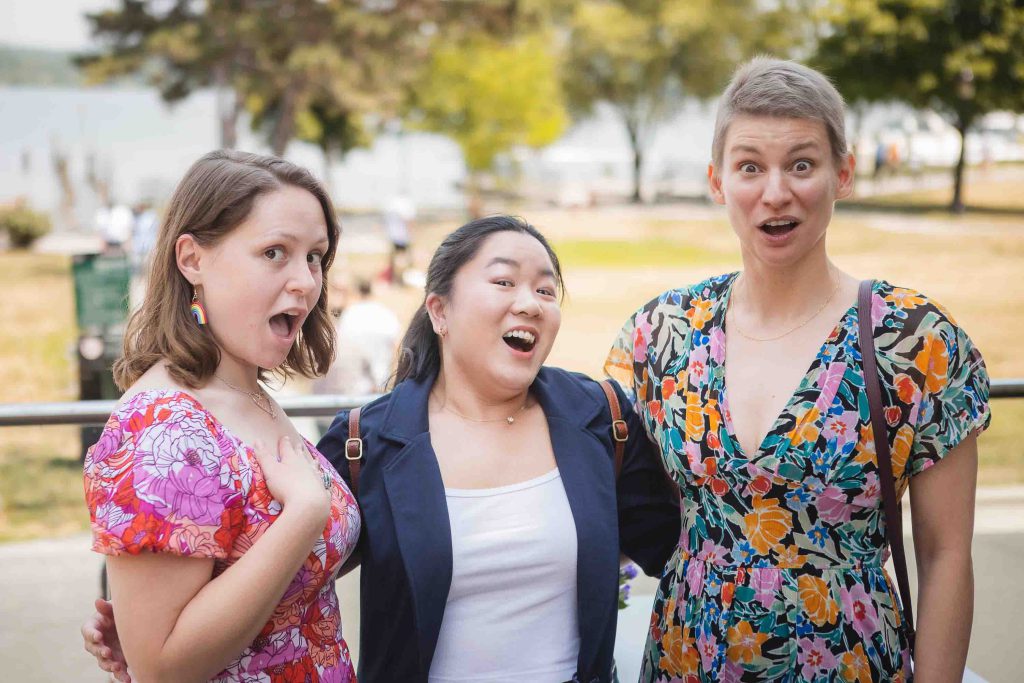 Three women with their mouths open at a lake during a birthday party.