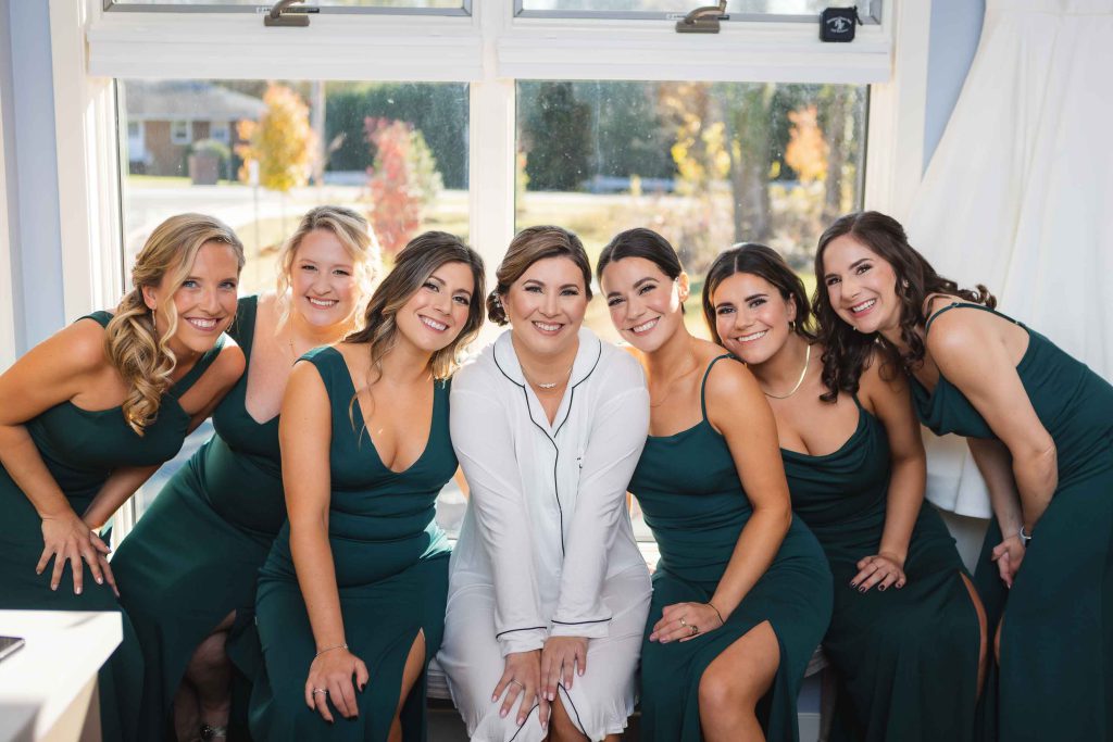 Bridesmaids in emerald dresses candidly posing for a photo during wedding preparations.