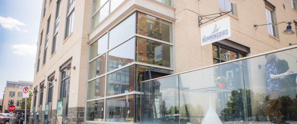 A glass facade building with a glass door located in Alexandria, Virginia for Hummingbird Bar & Kitchen.