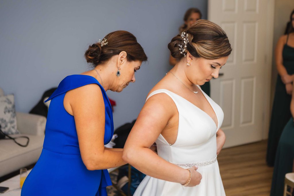 A bride assisting her mother during wedding preparations in a candid moment.