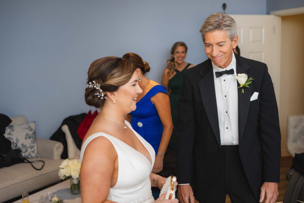 A candid wedding preparation moment captured of a man in a tuxedo and a woman in a dress.