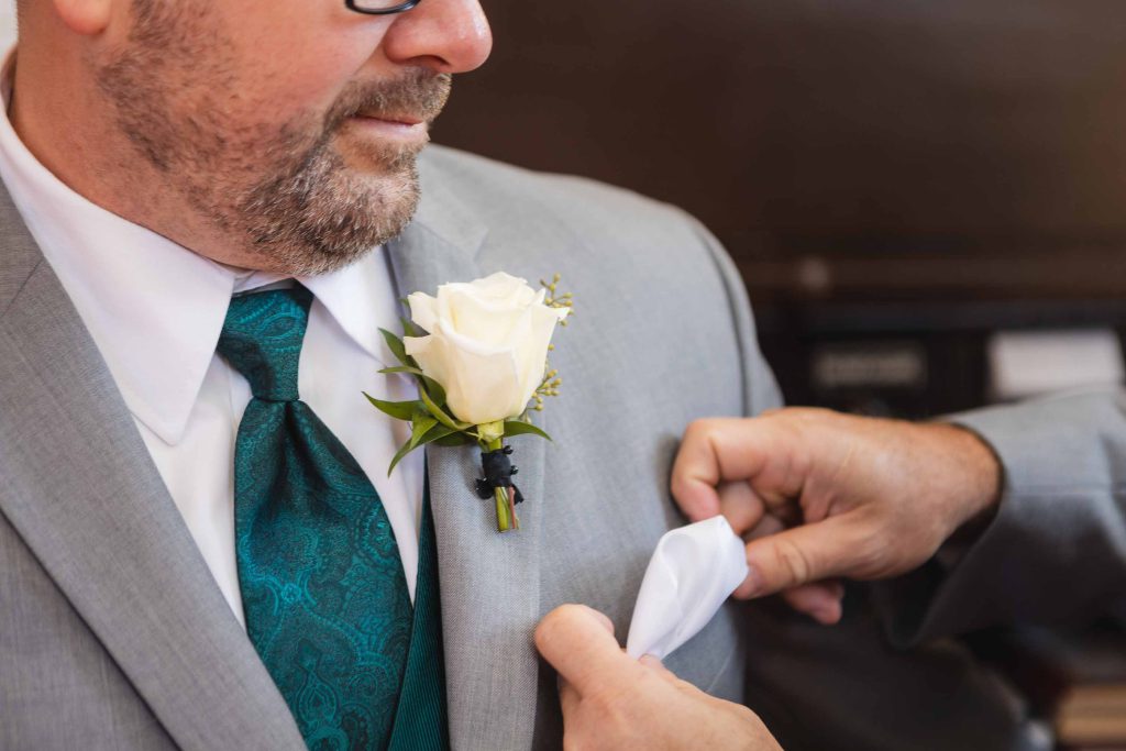 A candid man in a suit preparing for a wedding by putting on a boutonniere.