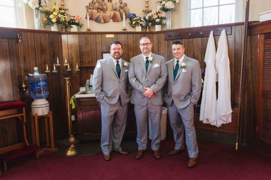 Three groomsmen candidly standing in front of a church during wedding preparation.