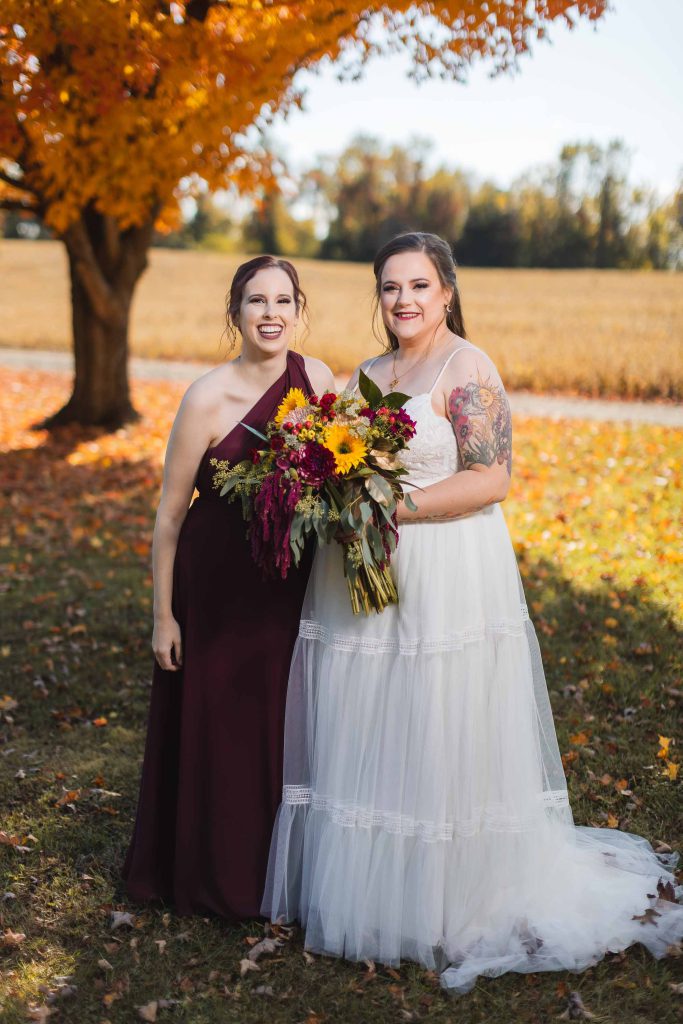 Two bridesmaids posing for a portrait in front of a fall tree at a wedding.