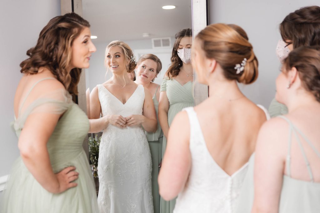 A bride and her bridesmaids prepare for their wedding, candidly admiring their reflection in the mirror.