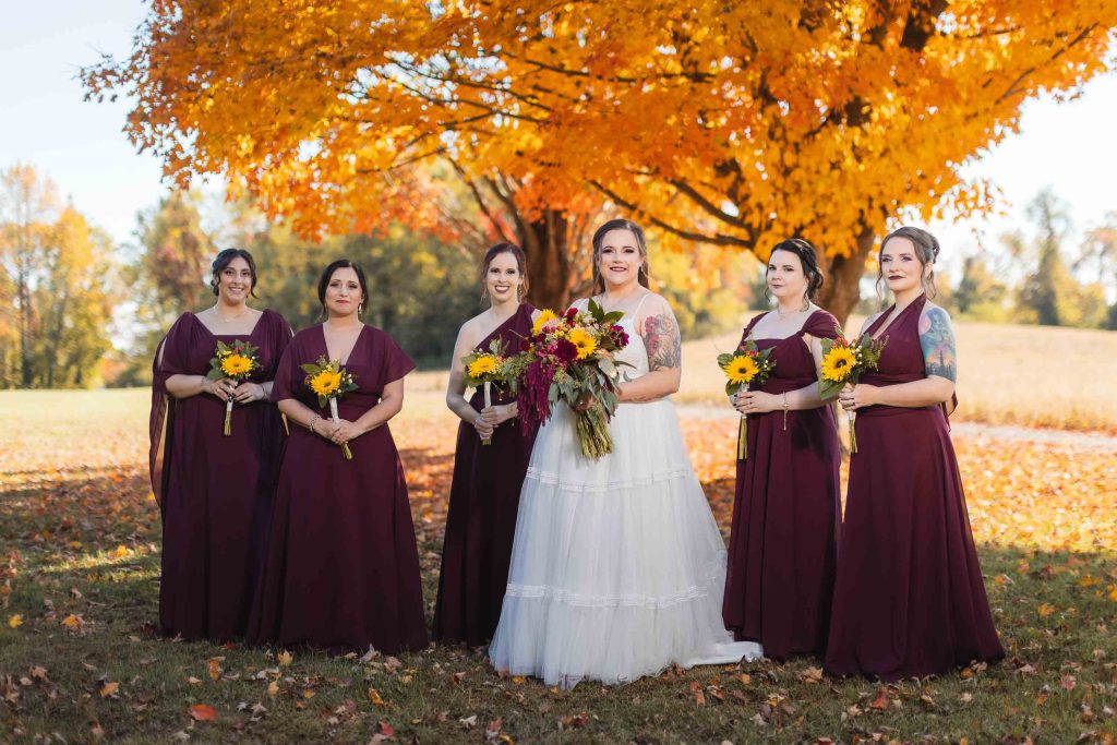 Burgundy bridesmaids posing in front of fall leaves at a wedding.