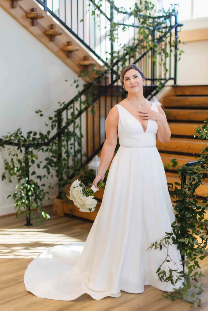 A bride in a white wedding dress standing in front of a staircase, captured in a stunning portrait.