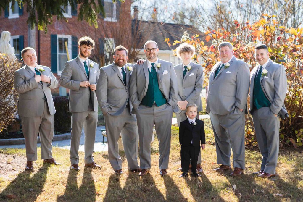 A group of groomsmen pose for a wedding portrait in front of a house.