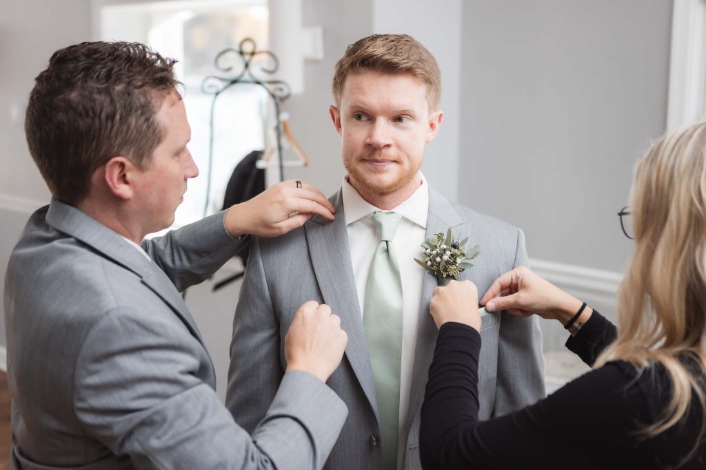 A candid man preparing a groom for the wedding by putting a boutonniere.