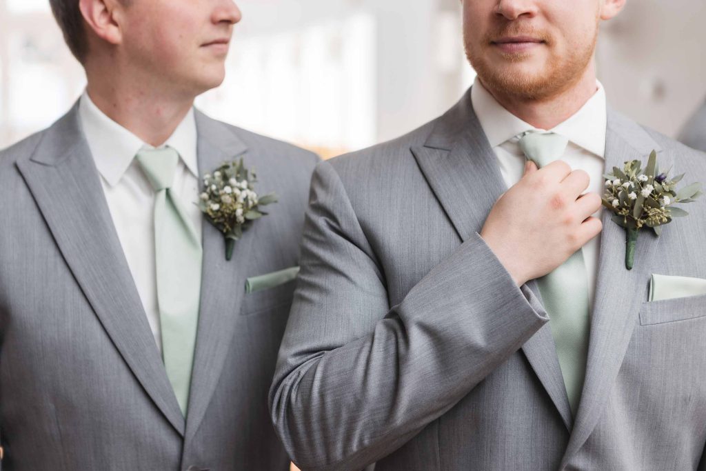 Two groomsmen preparing their boutonnieres for a candid wedding moment.