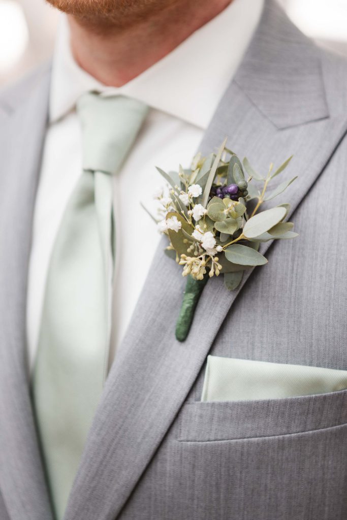 Detailed wedding attire showcasing a man in a grey suit with a green boutonniere.
