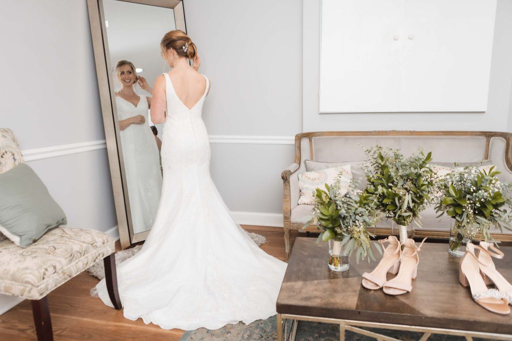 A candid bride is in preparation, looking at her wedding shoes in front of a mirror.