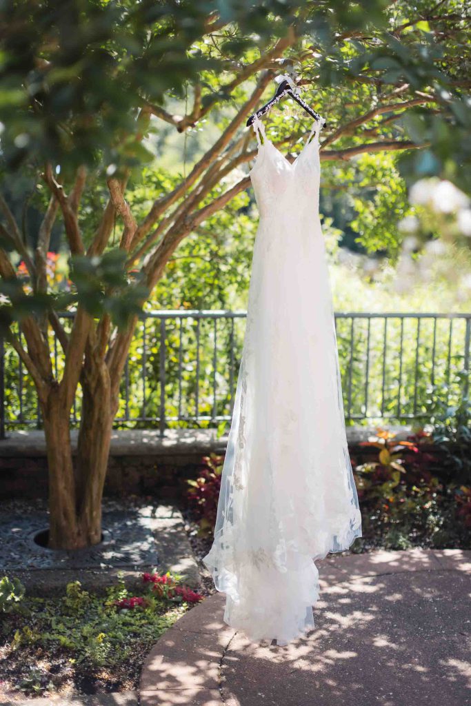 A detailed wedding dress hanging from a tree in a garden.