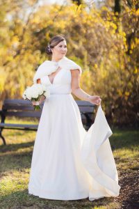 A wedding portrait of a bride in a white wedding dress standing in a park.