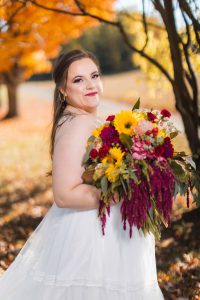 A bride in a wedding dress holding a bouquet during an autumn portrait session.
