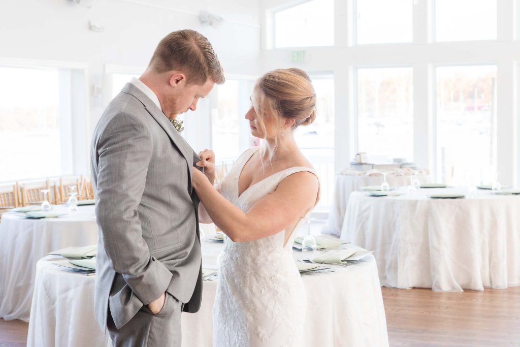 Candid wedding preparation as the bride and groom adjust each other's ties at the reception.