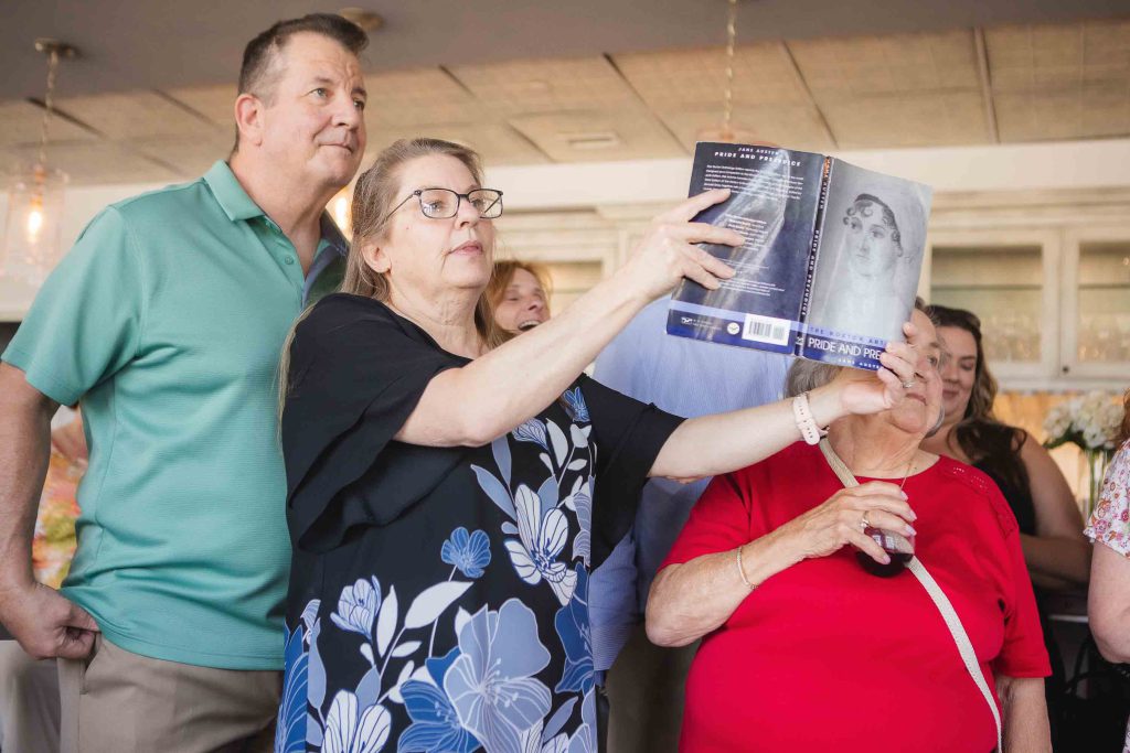 A group of people celebrating at a birthday party, looking at a photo of a baby.