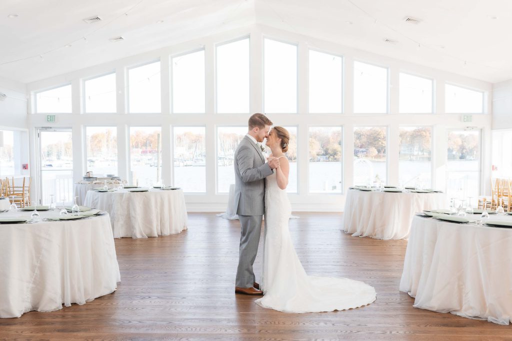 A candid wedding preparation moment with a bride and groom in a large room with windows.