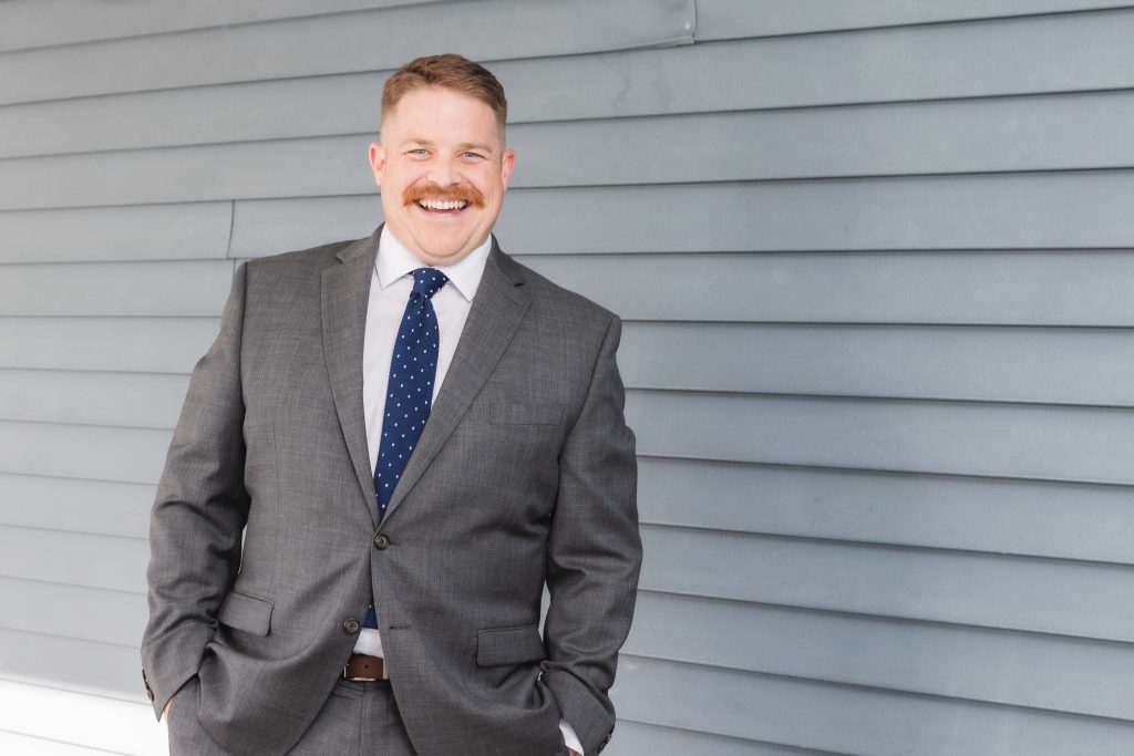 A man in a suit and tie is candidly leaning against a wall.