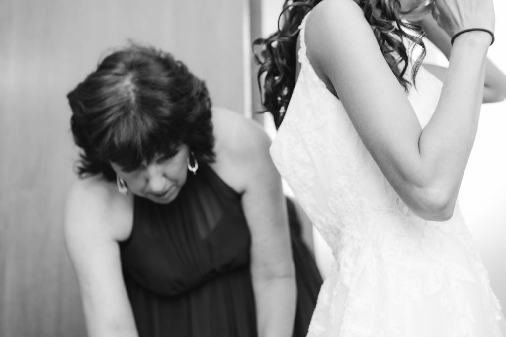 A candid woman assists her daughter in wedding dress preparations.