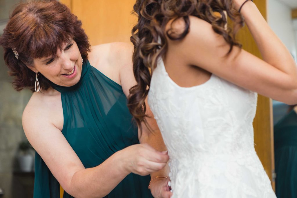 A bride assists her mother in candid wedding dress preparation.