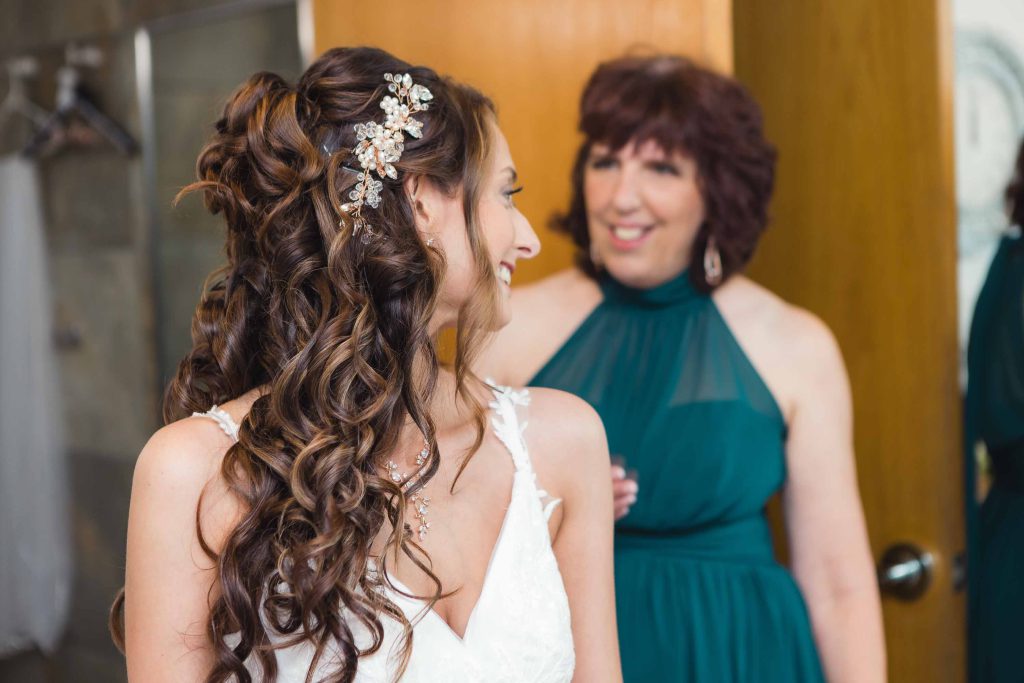 Preparation: A candid moment of a bride and her mother sharing a look in the mirror before the wedding.
