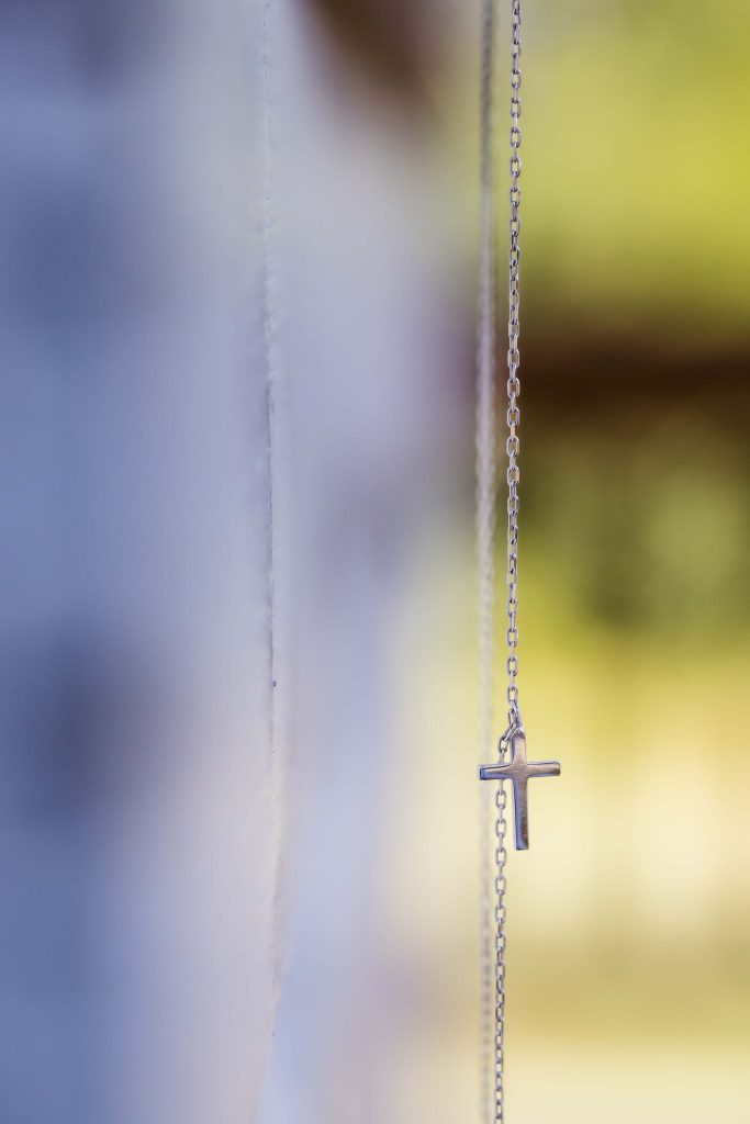 A silver cross pendant on a wedding chain.