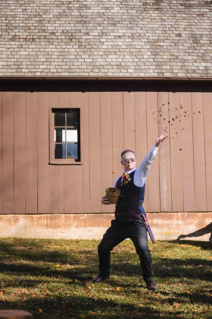 A man throwing a frisbee during a wedding ceremony in front of a barn.
