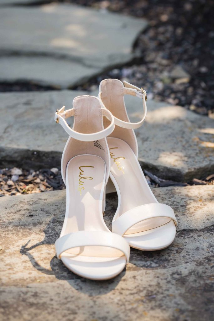 A pair of white wedding sandals sitting on a rock.