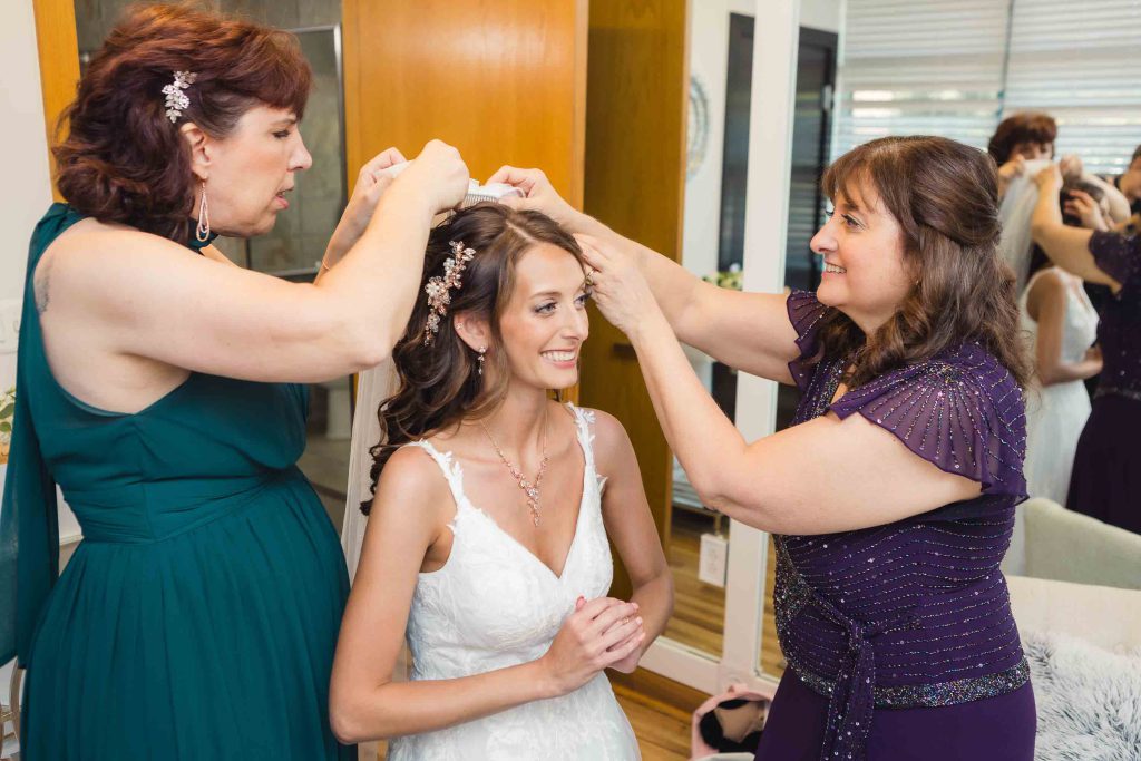 A candid wedding preparation moment of a bride getting her hair done by a bridesmaid.