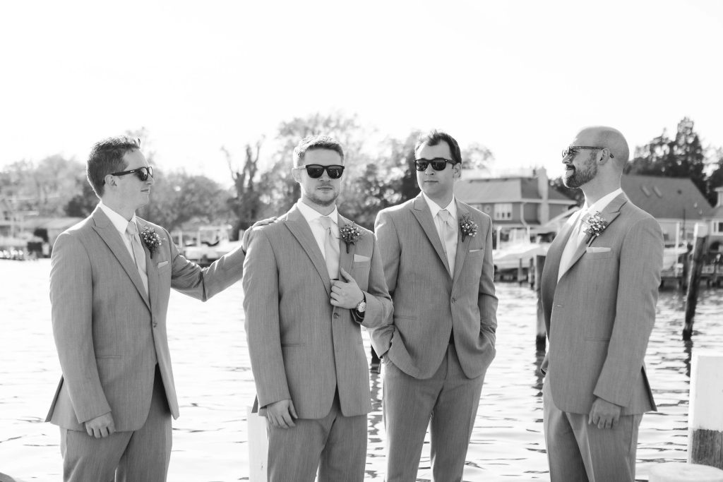 A group of groomsmen posing for a wedding portrait on a dock.