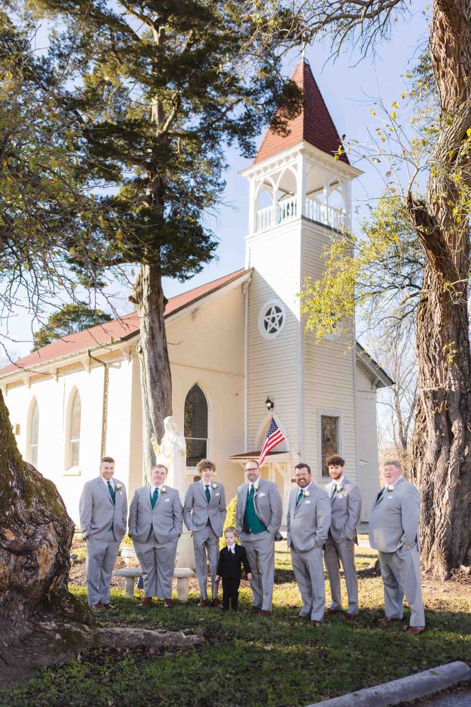 A group of groomsmen posing in front of a church for a wedding portrait.