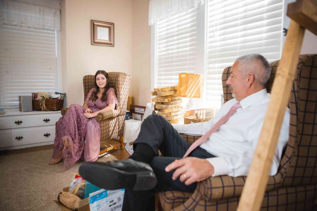 A couple sitting candidly in a cozy living room chair during wedding preparation.