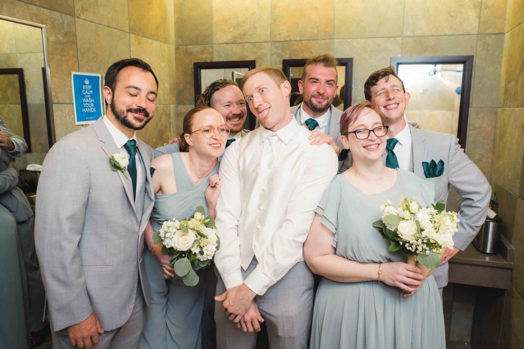 A candid group of groomsmen preparing for a wedding pose in a bathroom.