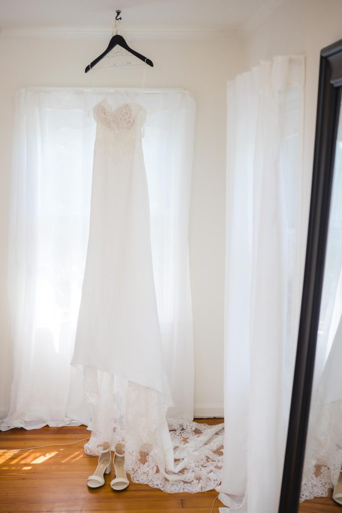 A wedding dress hangs in front of a mirror, showcasing intricate details.