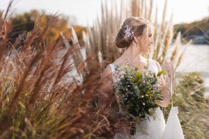 A bride in a wedding dress posing for a portrait amidst tall grass.