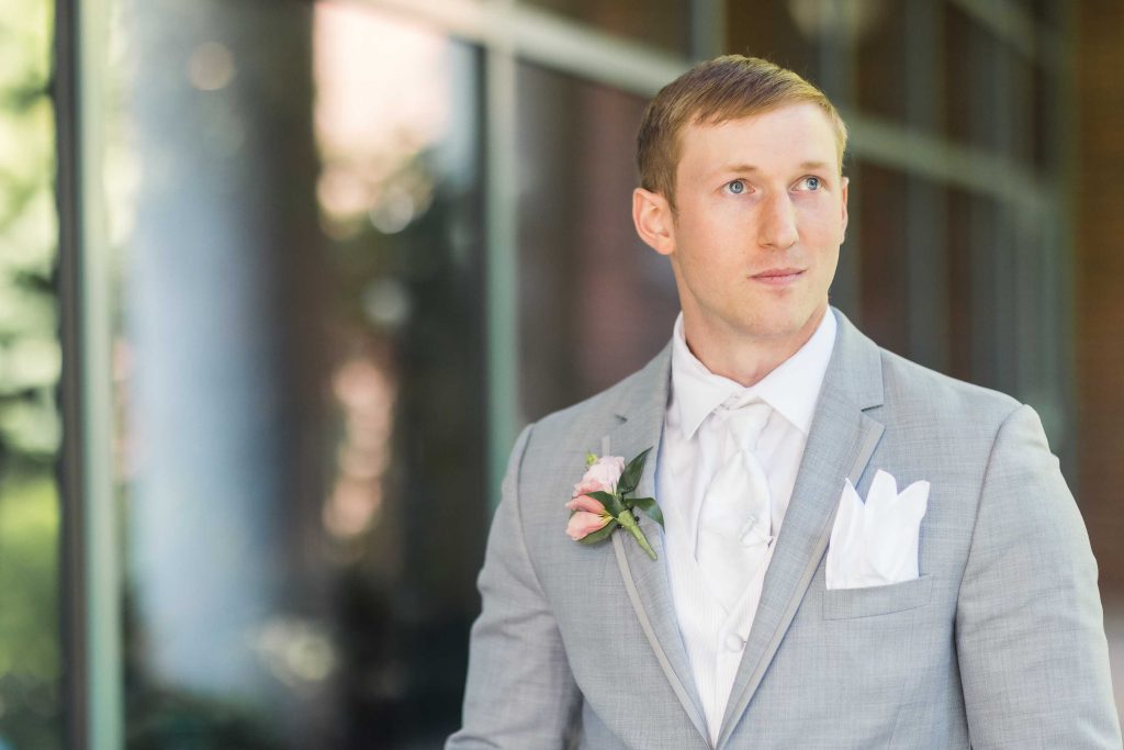 A man in a gray suit is candidly standing in front of a building.