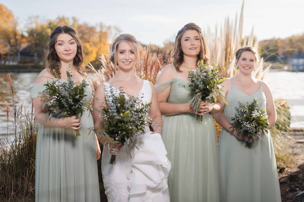 Four bridesmaids with bouquets in front of a lake at a wedding.