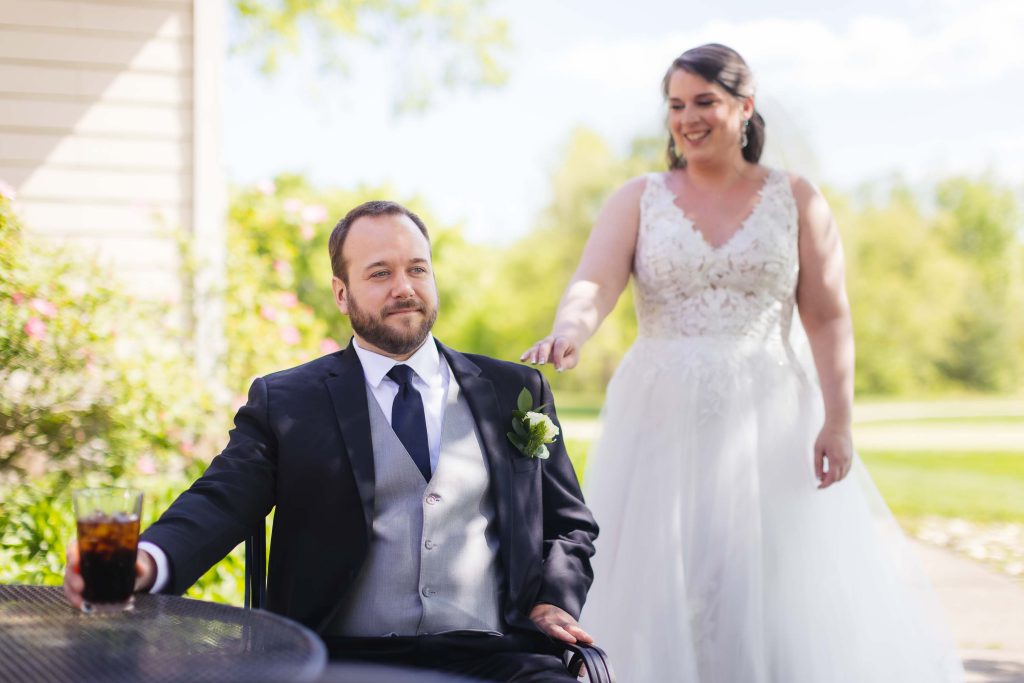 A candid wedding preparation with a bride in a wedding dress and a groom in a wheelchair.