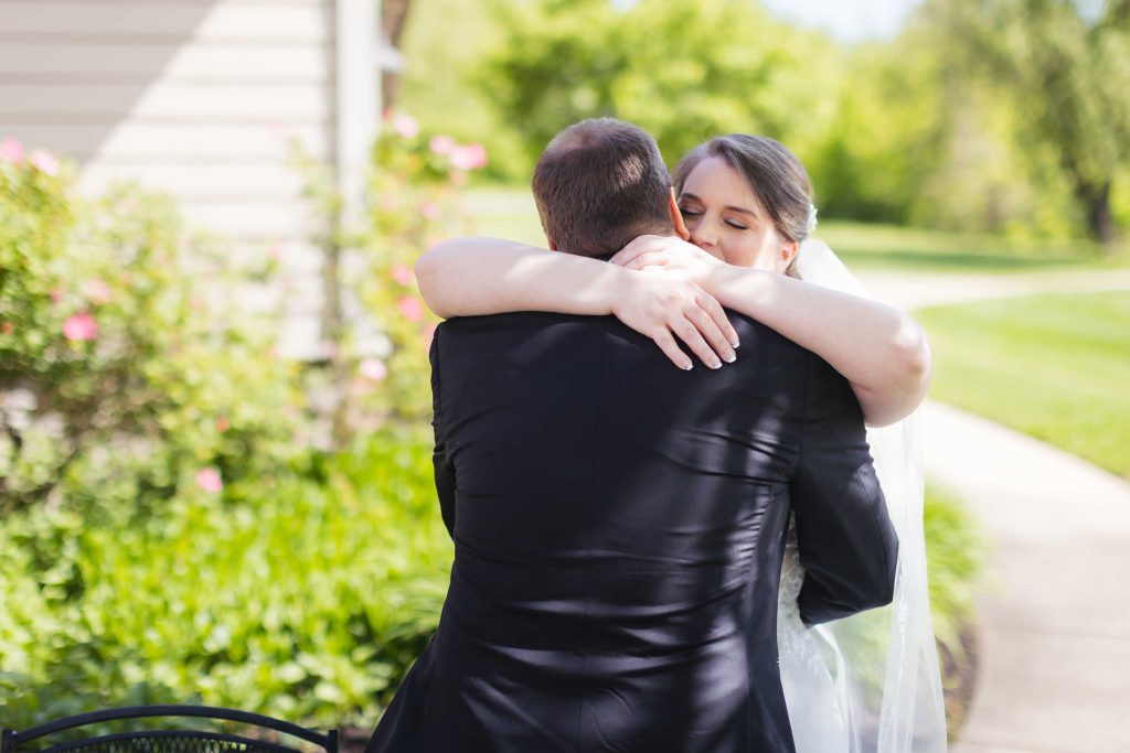 A candid bride and groom hugging in front of a house as part of their wedding preparations.