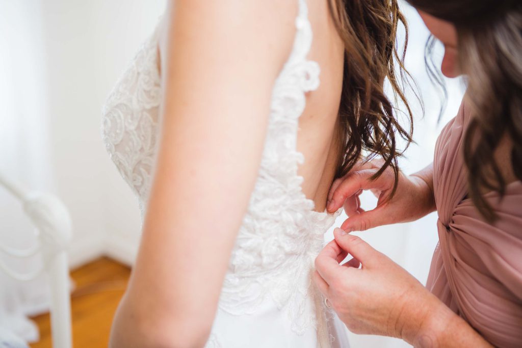 A candid moment of wedding dress preparation, as a woman carefully buttons the bride's gown.