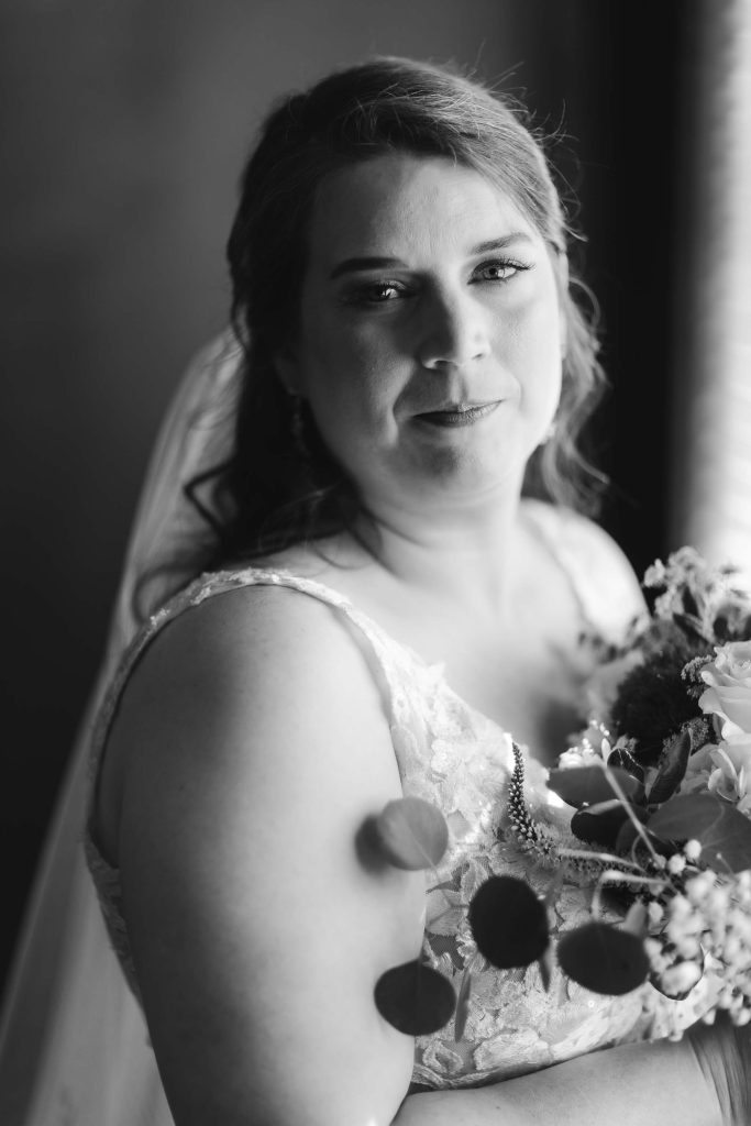 A black and white portrait of a bride holding her bouquet at her wedding.