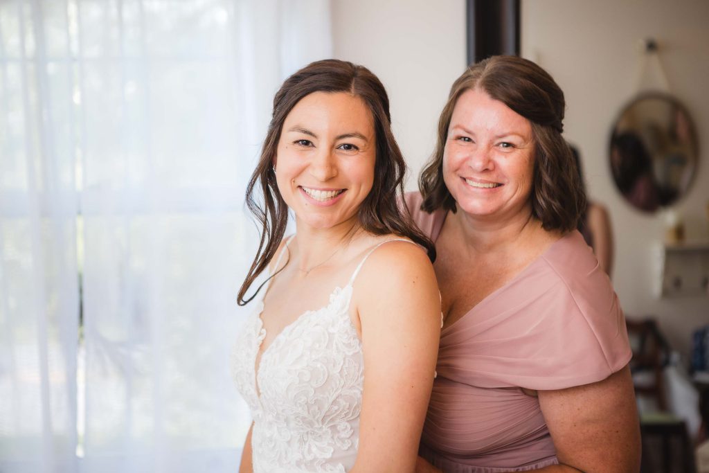 A candid bride and her mother posing for a photo during wedding preparation.