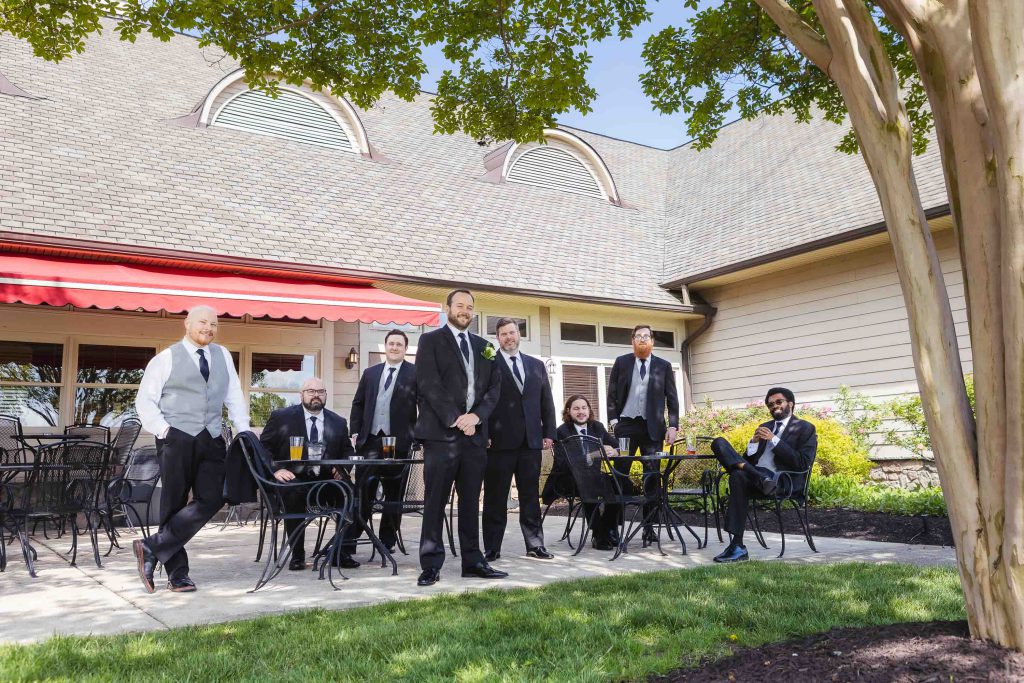 A group of groomsmen posing in front of a tree for a wedding portrait.